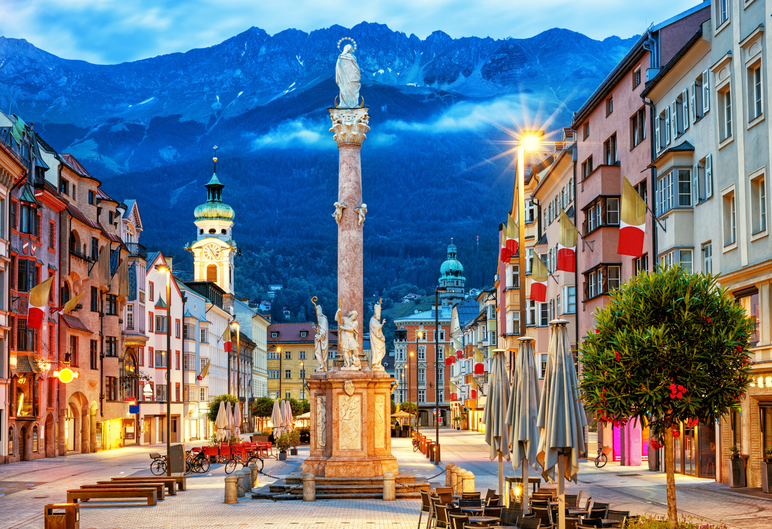 Old town in the alps with colourful houses on a square and a statue with saints.